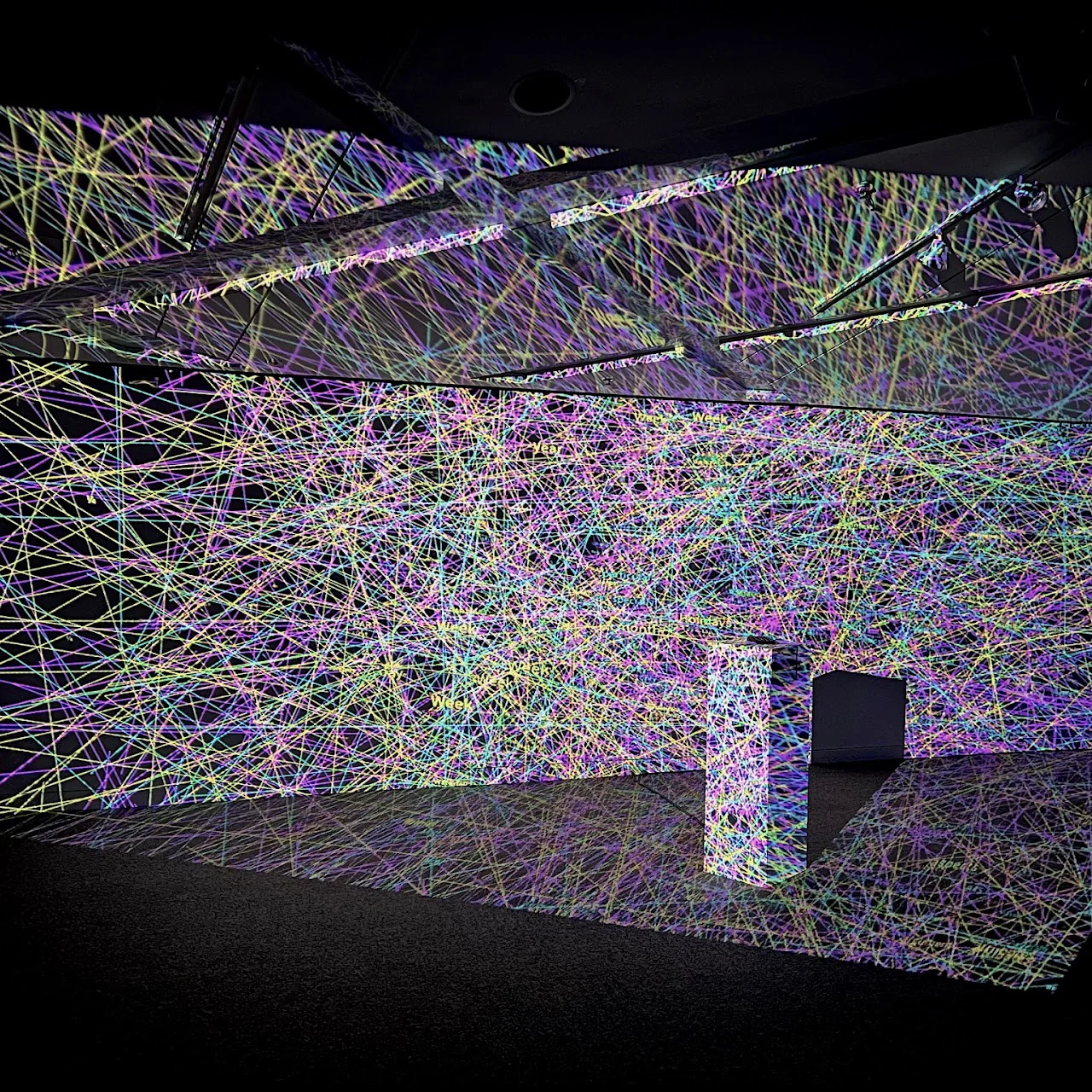 A room-scale projection filled with interlaced coloured lines and floating words.